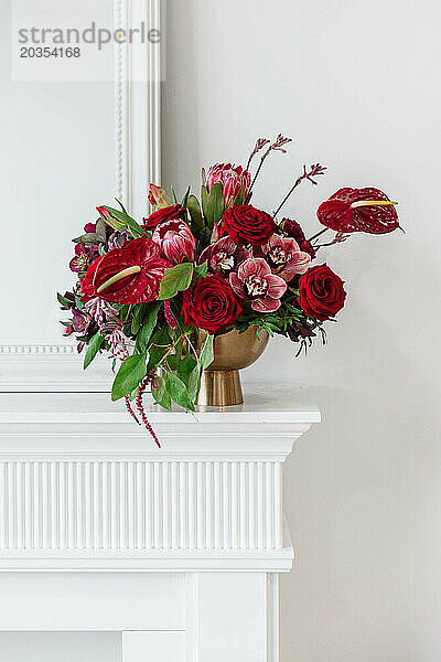 Lebendiges Blumenarrangement in großen Rottönen in einer goldenen Vase