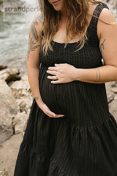Frau hält ihren Babybauch während eines Schwangerschaftsfotoshootings im Freien