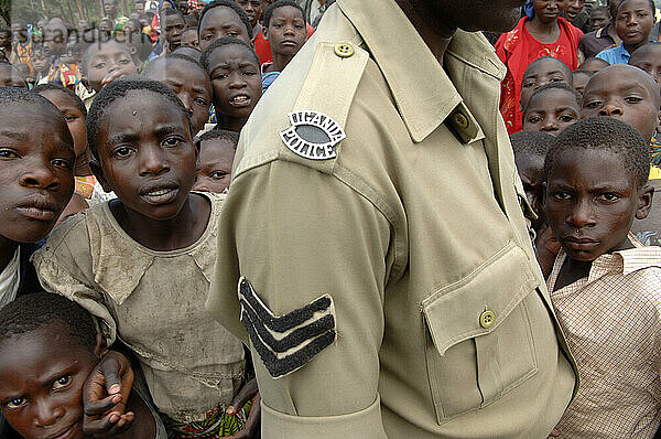 Refugee children stand behind a police officer.