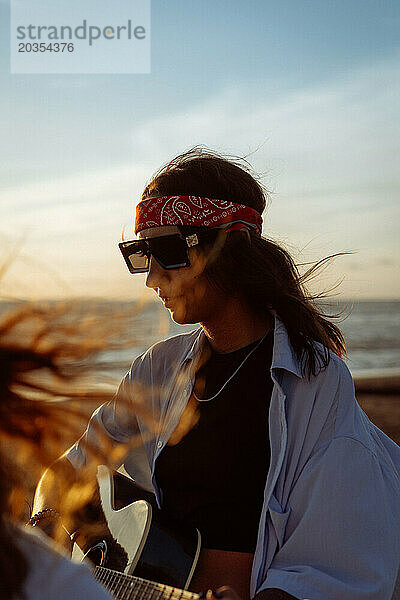 Musikerin singt und spielt Gitarre am Strand. In einem Bandana. Bali