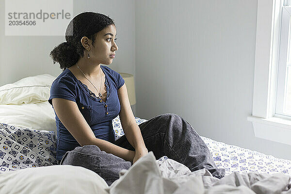 Ein gemischtrassiges Teenager-Mädchen sitzt auf einem ungemachten Bett und sieht deprimiert aus