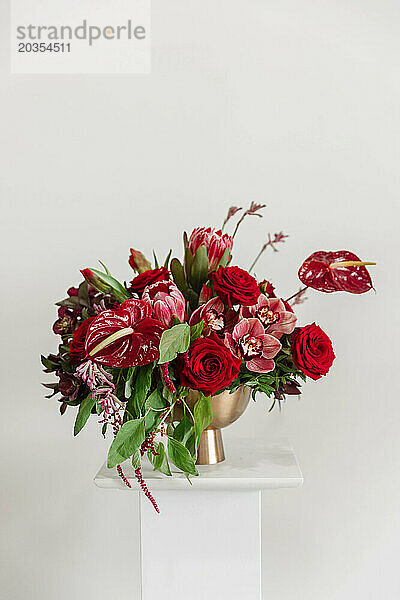 Lebendiges Blumenarrangement in großen Rottönen in einer goldenen Vase