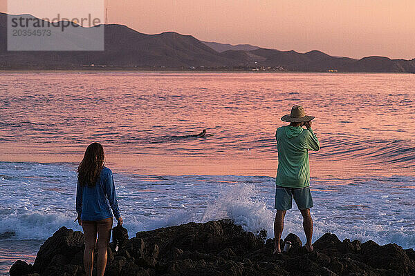 Ein Mann fotografiert Surfer bei Sonnenuntergang.