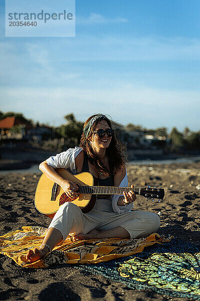 Musikerin singt und spielt Gitarre am Strand. In einem Bandana. Bali