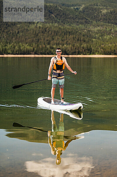 Mann genießt eine sonnige Paddleboarding-Session auf einem ruhigen Bergsee