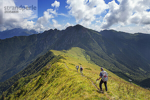 Drei männliche Wanderer (ältere Menschen) wandern auf einem grasbewachsenen Bergrücken in den italienischen Alpen.