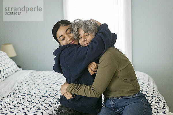 Eine weiße Mutter und ihre gemischtrassige Teenager-Tochter lächeln und umarmen sich im Schlafzimmer