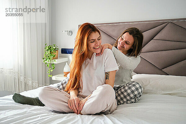 Brasilianerin massiert Schultern und Nacken ihrer Freundin im Bett.