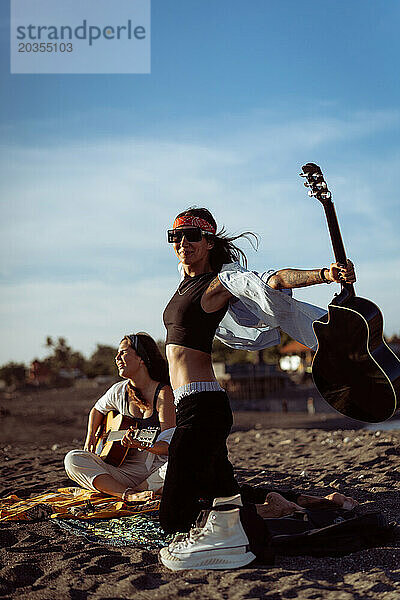 Musikerin singt und spielt Gitarre am Strand. In einem Bandana. Bali