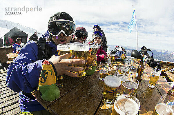 Skifahrer und Snowboarder feiern einen sonnigen Tag auf dem Hügel des Cerro Catedral mit Bier