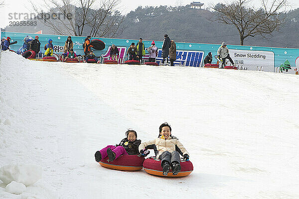 Asiatische Frau und ihre Tochter haben Spaß beim Rodeln steilen Eishangs  Hwacheon Sancheoneo Ice Festival  Gangwon-do  Südkorea