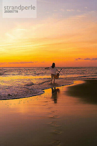 Musikerin mit Gitarre am Strand bei Sonnenuntergang. Bali