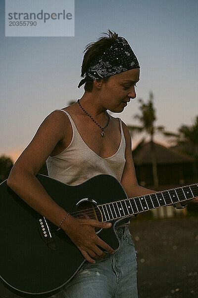 Musikerin singt und spielt Gitarre am Strand. In einem Bandana. Bali