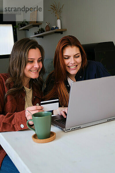 Lesbisches Paar kauft online mit Kreditkarte und Laptop zu Hause ein.