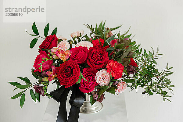 Lebendiges Blumenarrangement in großen Rottönen in einer goldenen Vase