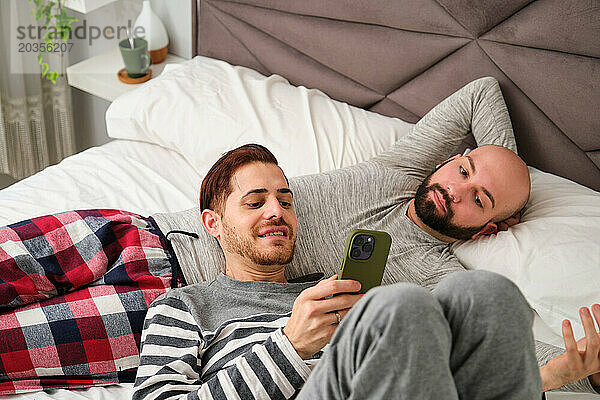 Homosexuelles Paar telefoniert gemeinsam und entspannt im Bett.