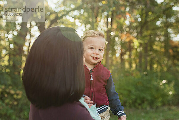 Rückansicht einer Mutter  die ihren lächelnden kleinen Sohn in einem Naturpark hält