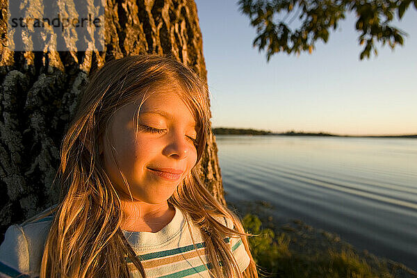 Ein junges Mädchen ruht bei Sonnenuntergang am Lake Seymour in Ontario  Kanada  an einem Baum.