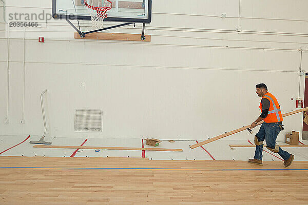 Ein Arbeiter verlegt einen Ahornholzboden auf einem Basketballplatz.