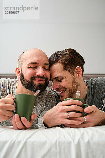 Schwules verliebtes Paar trinkt gemeinsam Kaffee im Bett.