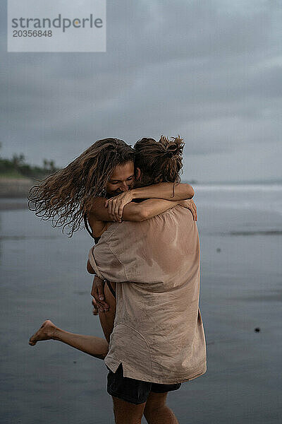 Junges  fröhliches  verliebtes Paar  das sich am Strand umarmt.