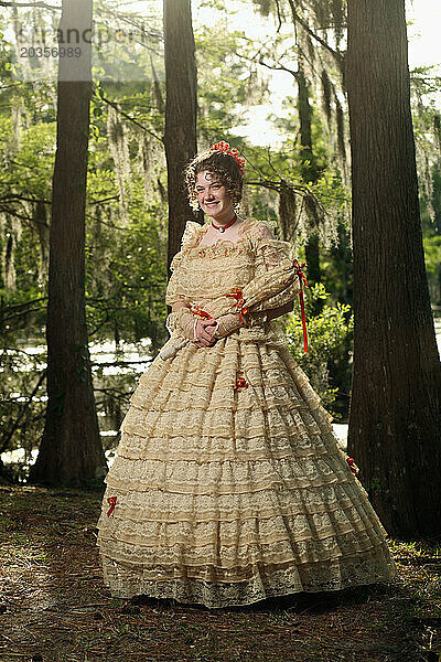 Eine junge Frau posiert in einem Southern Belle-Outfit  einschließlich eines großen  verzierten historischen Kleides und Sonnenschirms  in der Nähe eines Sees.