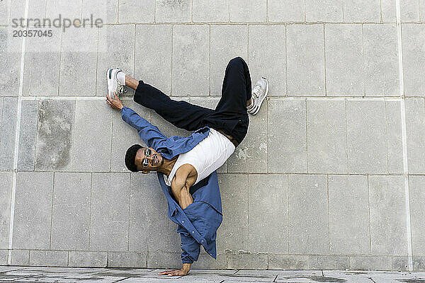 Junger cooler männlicher Tänzer  der Breakdance auf städtischem Mauerhintergrund aufführt.