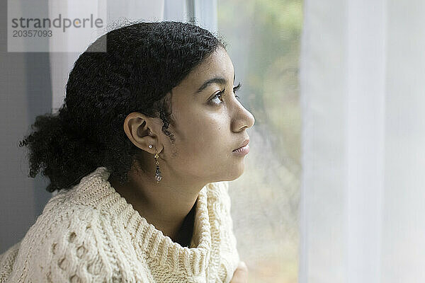 Biraciales Teenager-Mädchen am Fenster sieht deprimiert aus
