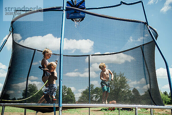 Drei Kinder spielen im Sommer draußen auf einem Trampolin mit Schlauch