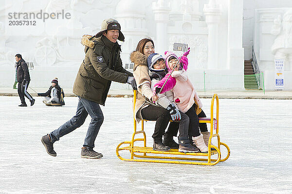 Familie hat Spaß daran  beim Hwacheon Sancheoneo Ice Festival  Gangwon-do  Südkorea  ein Selfie auf einem Gruppenschlitten auf dem zugefrorenen Fluss zu machen