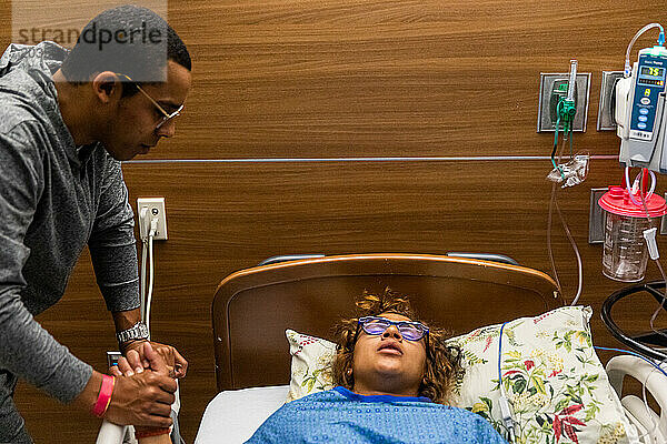 Gemischtrassiges Paar hält sich während der Wehen bei der Geburt im Krankenhaus an den Händen