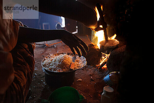 Eine tansanische Frau bereitet das Abendessen auf einem traditionellen Dreisteinofen zu