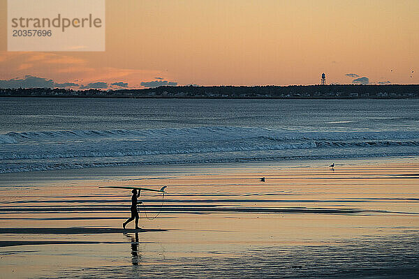 Silhouette eines Surfers  der mit einem Surfbrett am Strand spaziert