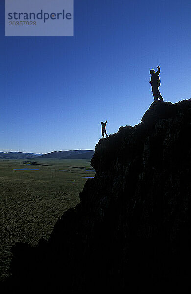 Zwei Menschen stehen mit erhobenen Armen am Rand einer Klippe in der Nähe des Firth River im Yukon-Territorium  Kanada.