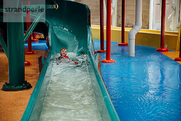 Weitblick auf einen kleinen Jungen  der im Indoor-Park die Wasserrutsche herunterkommt.