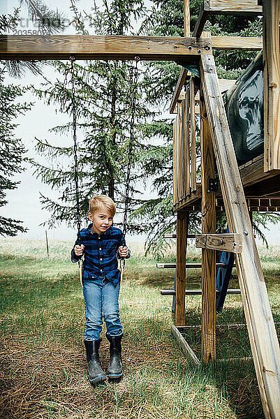 Weite Sicht auf einen kleinen Jungen  der auf einer Holzschaukel in einem ländlichen Land sitzt.