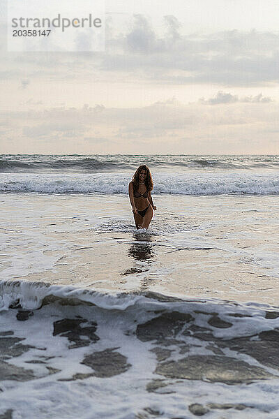 Porträt einer fröhlichen jungen Frau mit glücklichem lockigem Haar am Strand. Bali