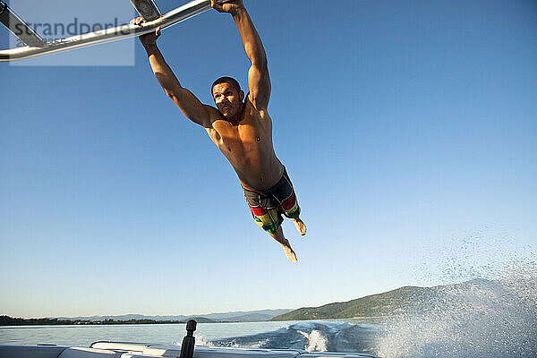Ein glücklicher junger Mann  der sich an einem Turm festhält und hinter einem Wakeboard-Boot in Idaho fliegt.