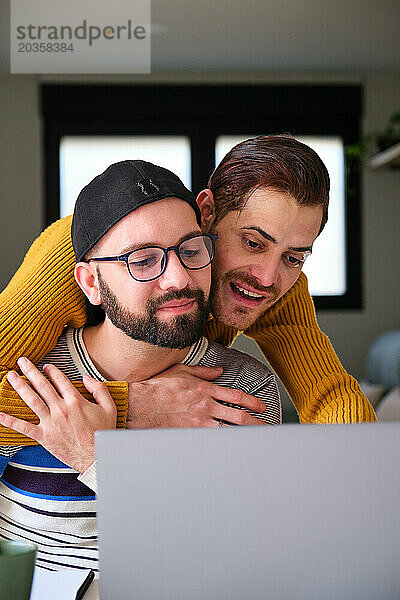 Homosexuelles Paar benutzt gemeinsam den Laptop und umarmt sich.