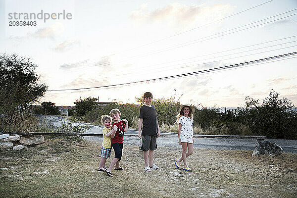 Vier glückliche Geschwister posieren gemeinsam bei Sonnenuntergang im Urlaub in Anguilla