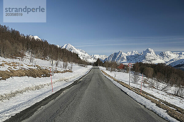 Leere Straße inmitten schneebedeckten Landes  die in Richtung Berge führt