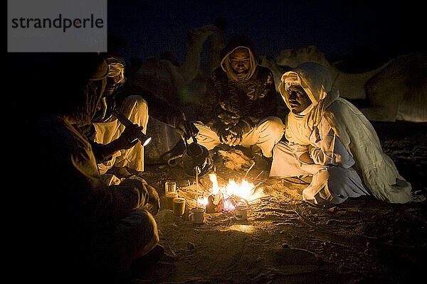 Kamelhirten treffen sich abends zum Abendessen  während sie mit einer Kamelkarawane durch die Sahara im Sudan reisen.