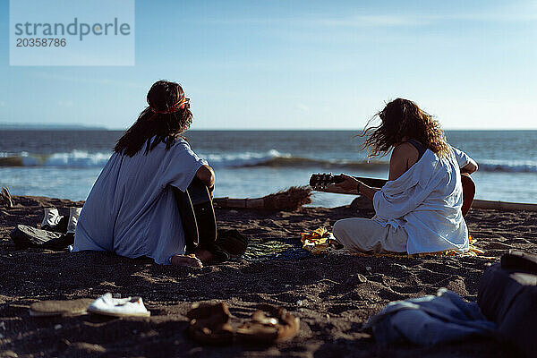 Freundinnen spielen Gitarren am Strand. Sonnenuntergang am Meer. Bali