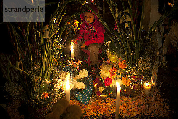 Ein Junge sitzt während der Feierlichkeiten zum Tag der Toten in Mexiko-Stadt in einem mit Kerzen und gelben Ringelblumen geschmückten Grab