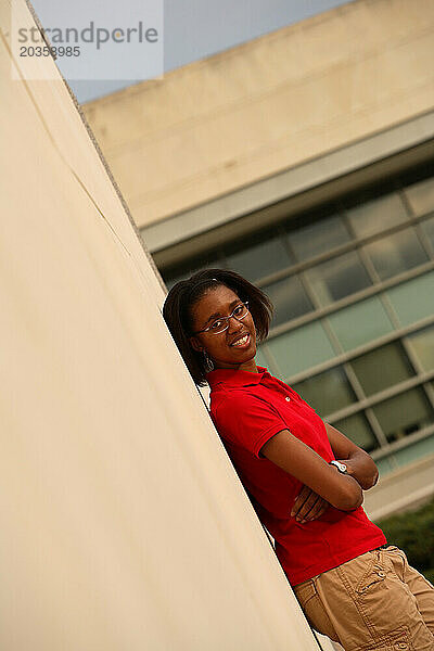 Portrait of a young black female student leaning against a wall on campus.