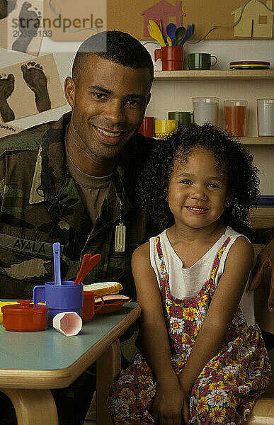 Ein afroamerikanischer Mann  der beim Militär ist  posiert mit seiner Tochter im Vorschulalter.