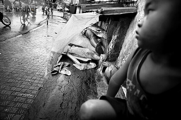 Sohn beobachtet Passanten  die darauf warten  dass Mutter aufwacht  in Hanoi  Vietnam.