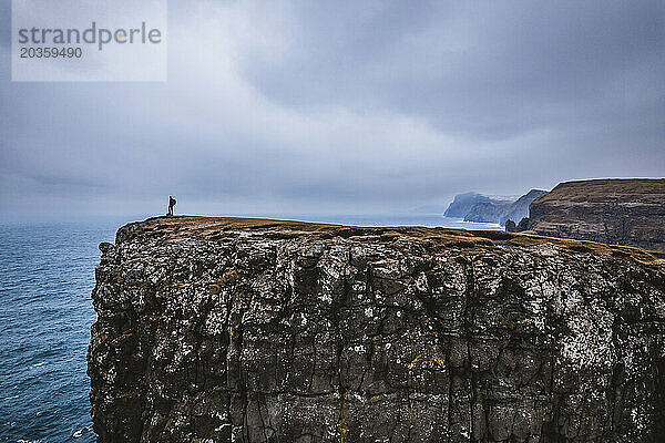 Einsamer Wanderer steht allein am Rand einer gewaltigen Meeresklippe auf den Färöer-Inseln
