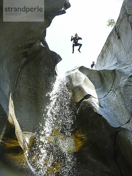 Mann im Neoprenanzug springt von einer Klippe neben dem Wasserfall  Cresciano  Kanton Tessin  Schweiz