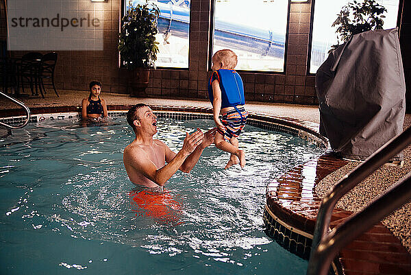 Kleinkind springt Papa in die Arme  während es drinnen im Pool spielt